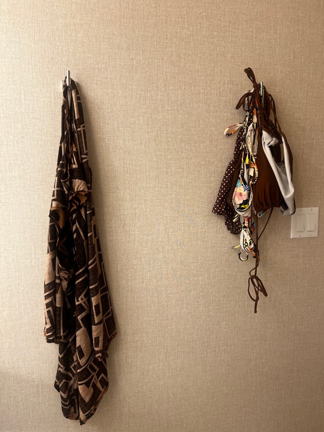 brown dress hanging on the left hook in the bathroom. One brown bikini and multi print bikini hanging on the same right hook.